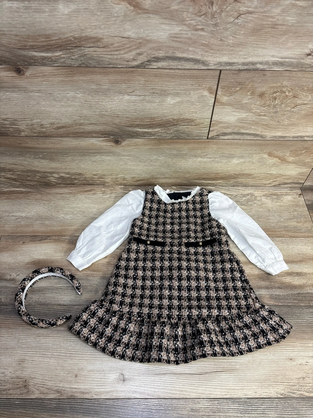 Girls black and beige checkered dress with white puff sleeves and matching checkered headband on wooden floor