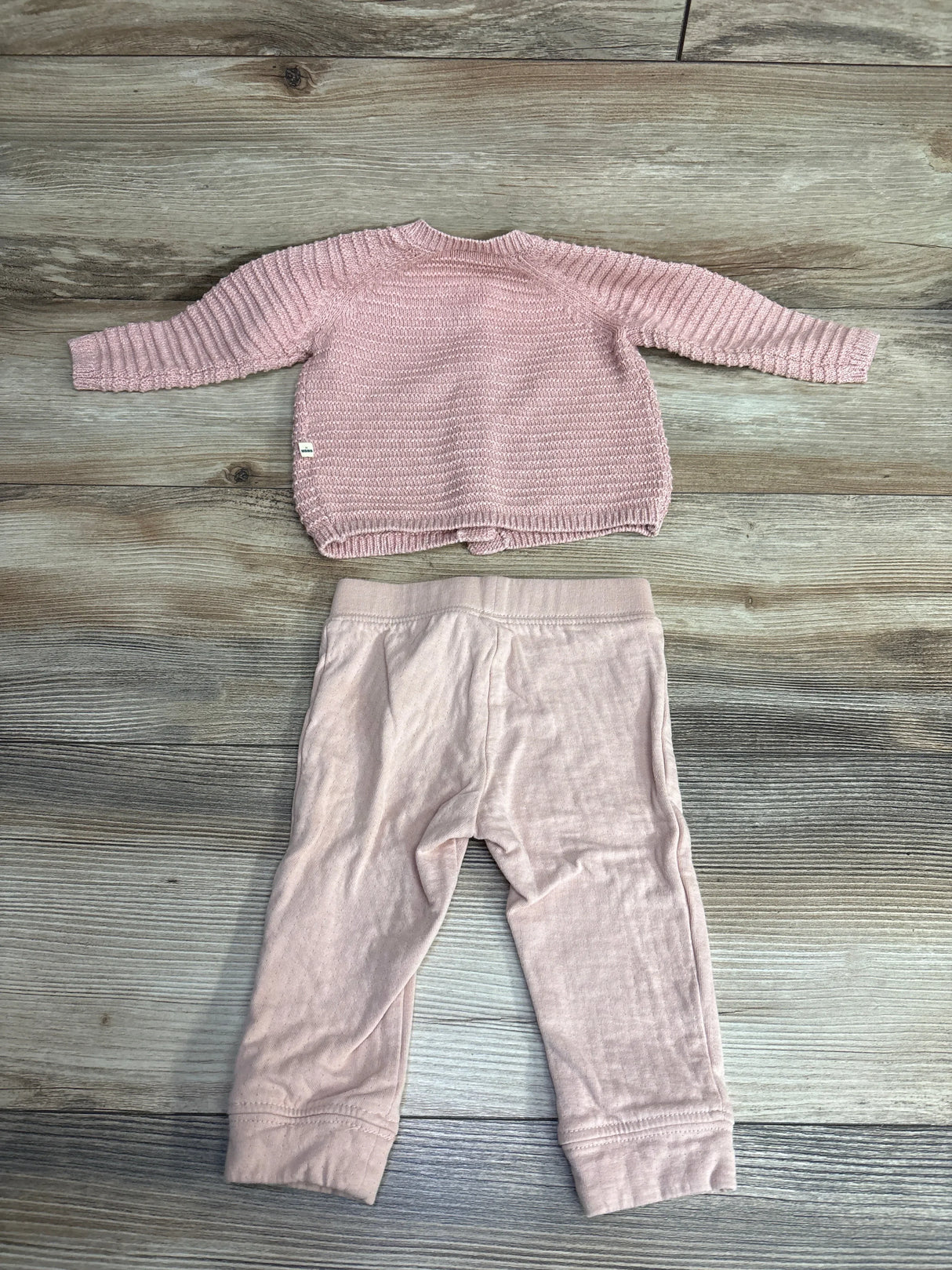 Pink knit baby sweater and matching pants set on wooden background