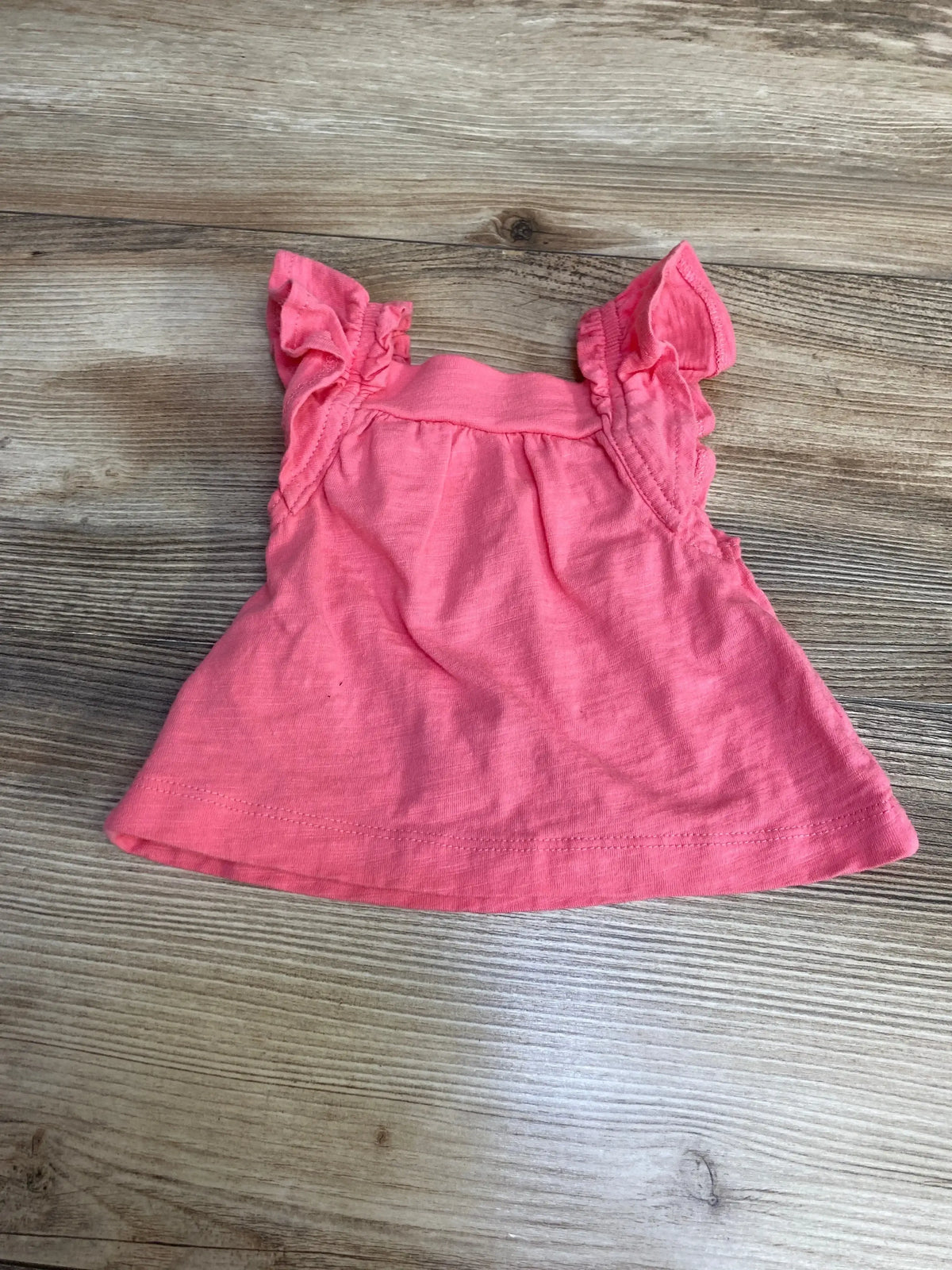 Flat lay of Carter’s newborn pink sleeveless top with ruffled flutter sleeves and gathered waist on wood background