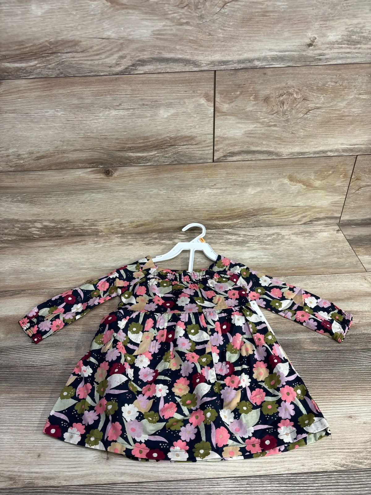 Long sleeve baby dress with colorful floral print, laid flat on wood background