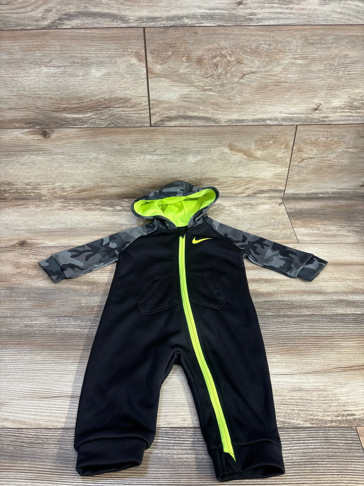 Top-down view of black Nike Dri-Fit hooded coverall with gray camo sleeves, neon yellow zipper and hood lining on wood floor