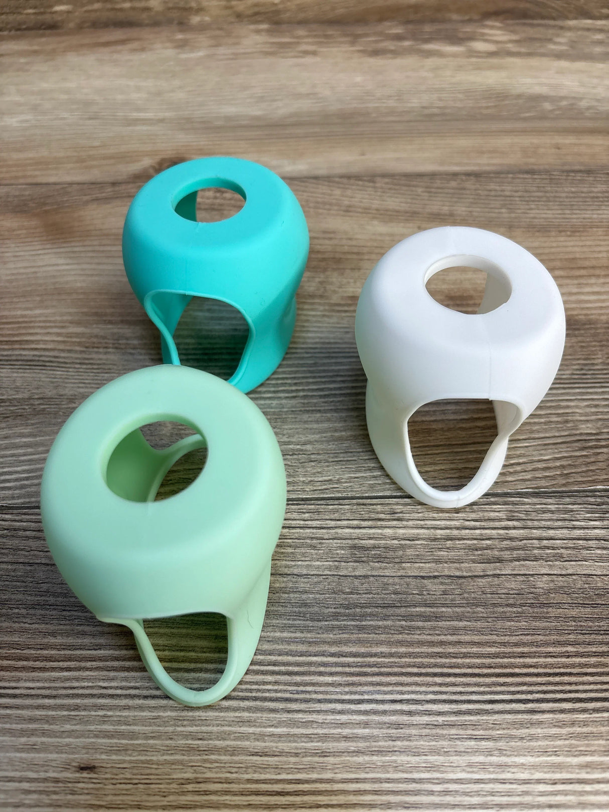 Three silicone baby bottle handles in mint, teal, and white on wood surface