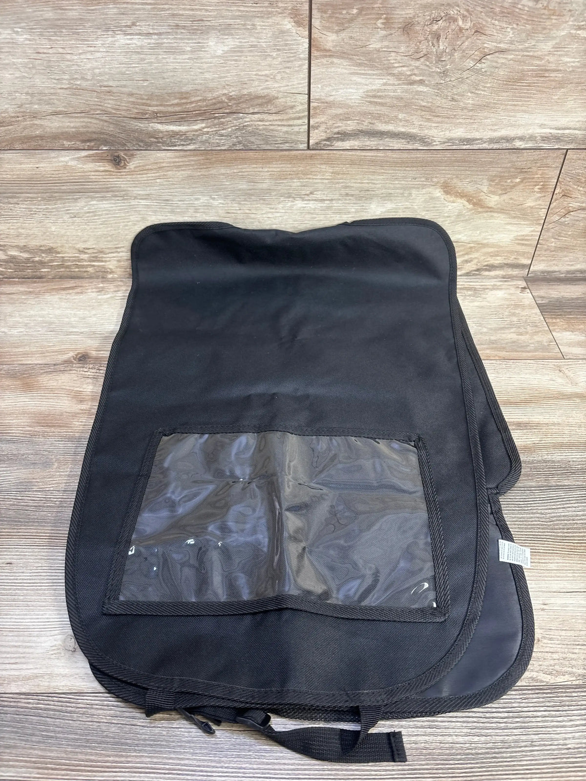 Top-down view of Nuby x Safe in the Seat car seat protector showing clear plastic storage pocket and straps on wood floor