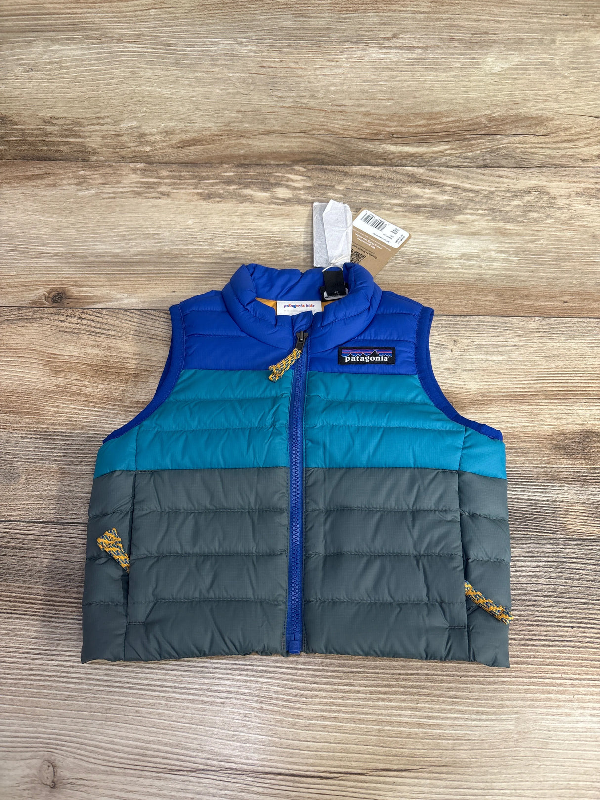 Patagonia kids' sleeveless puffer vest in blue, teal, and gray on wooden surface with zipper and logo