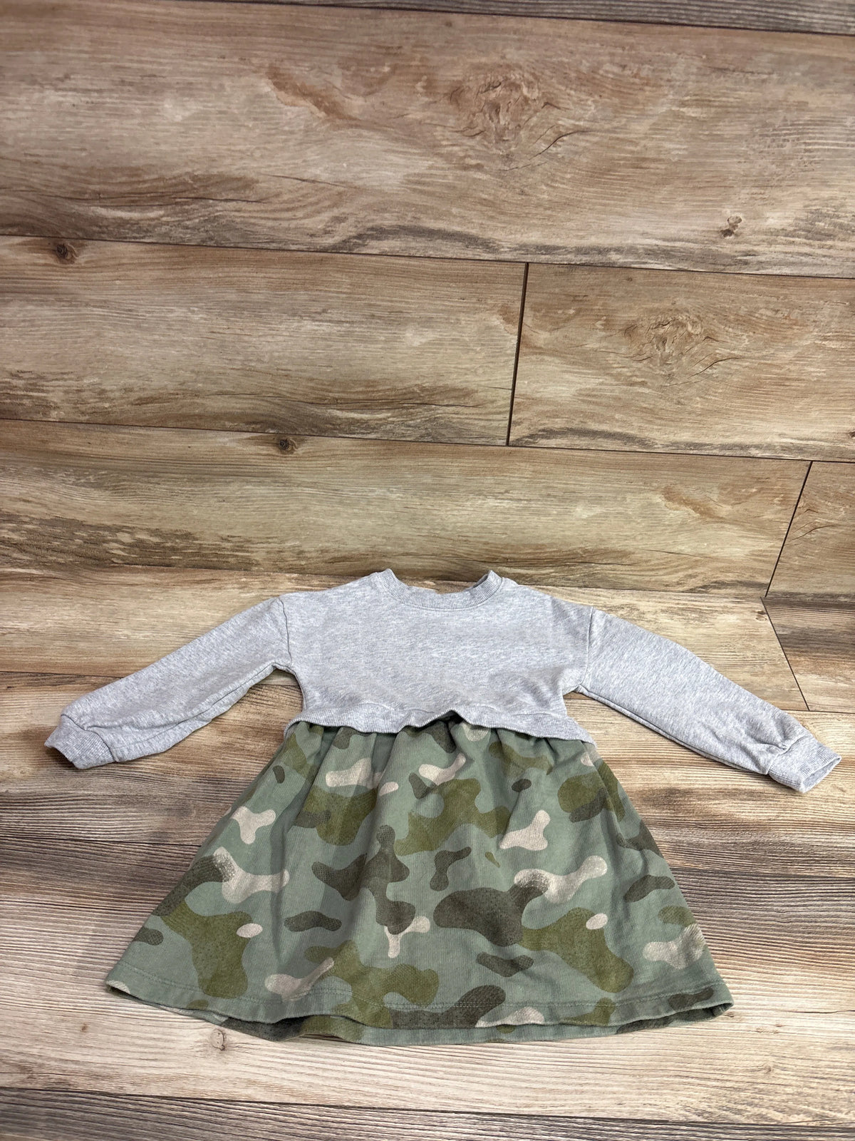 Front view of Carter’s grey sweatshirt dress with camouflage skirt and long sleeves on a wood floor