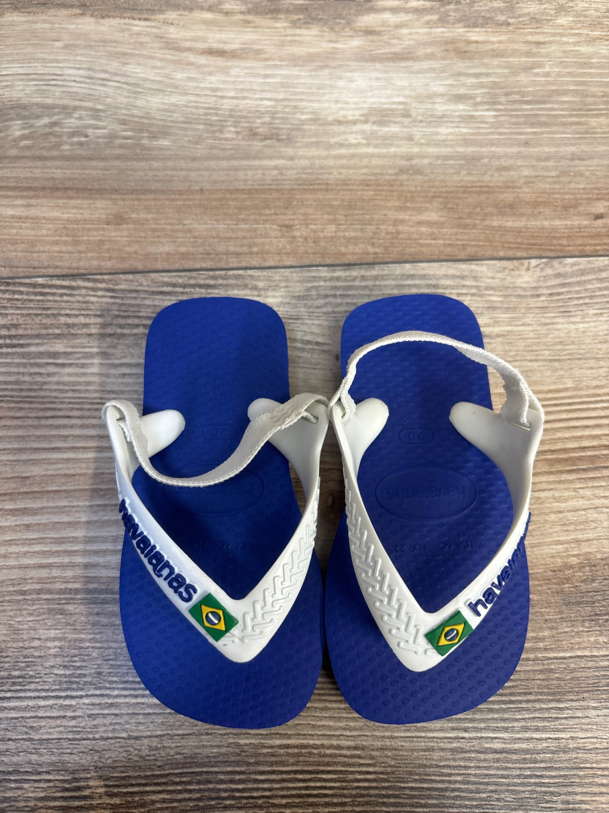 Blue and white Havaianas baby sandals with Brazil flag detail on wood background