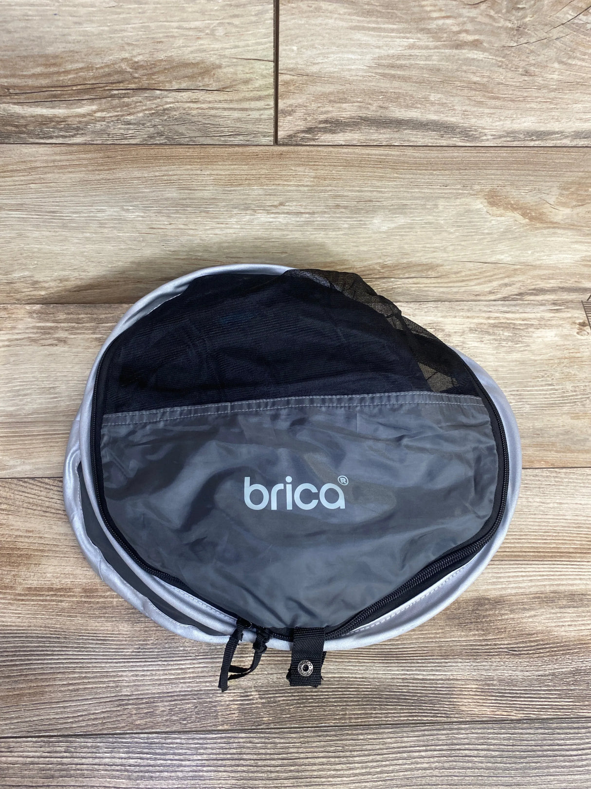 Folded Brica travel baby gear in gray with zippered mesh pouch on wood floor