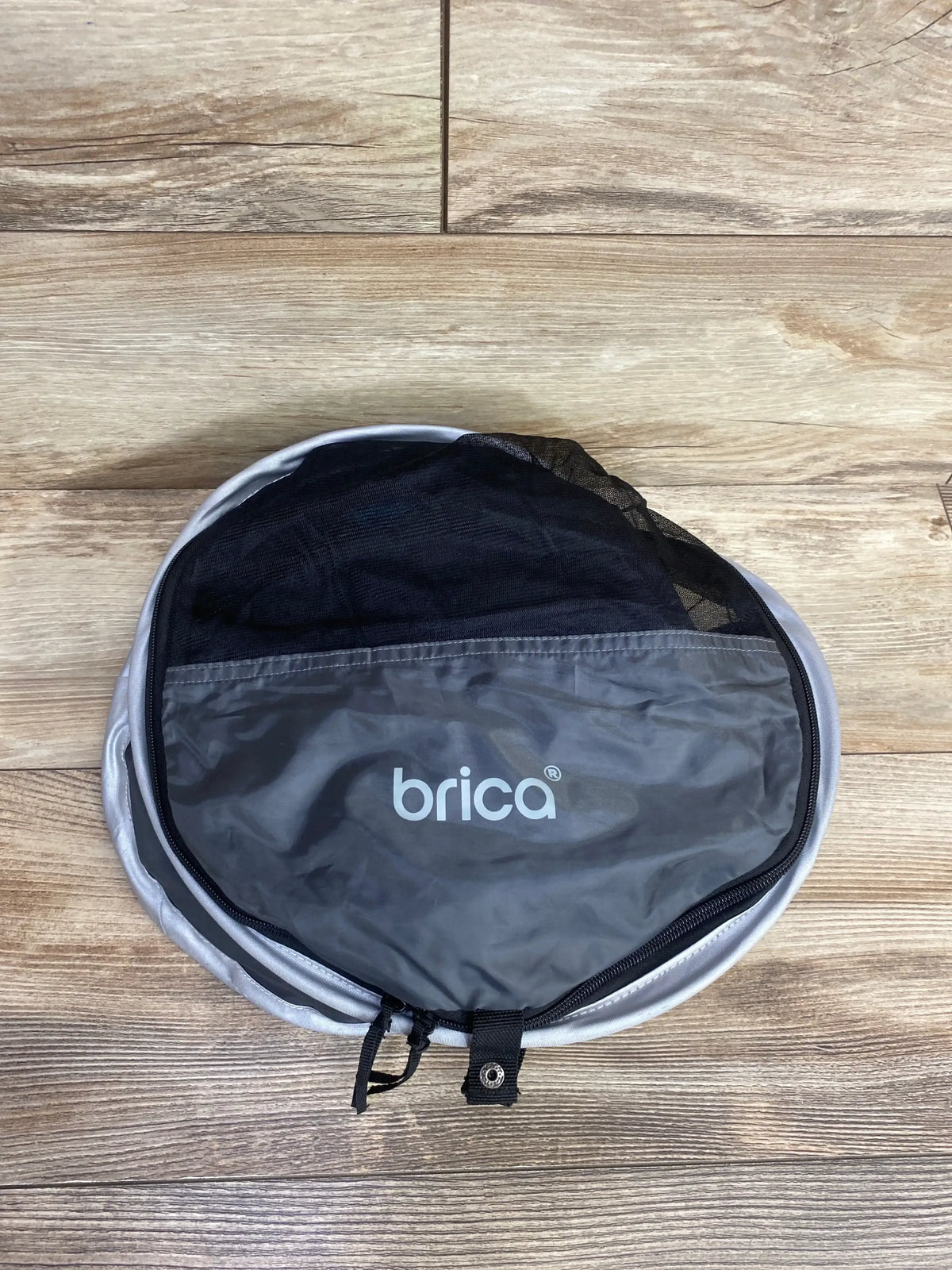 Folded Brica travel baby gear in gray with zippered mesh pouch on wood floor