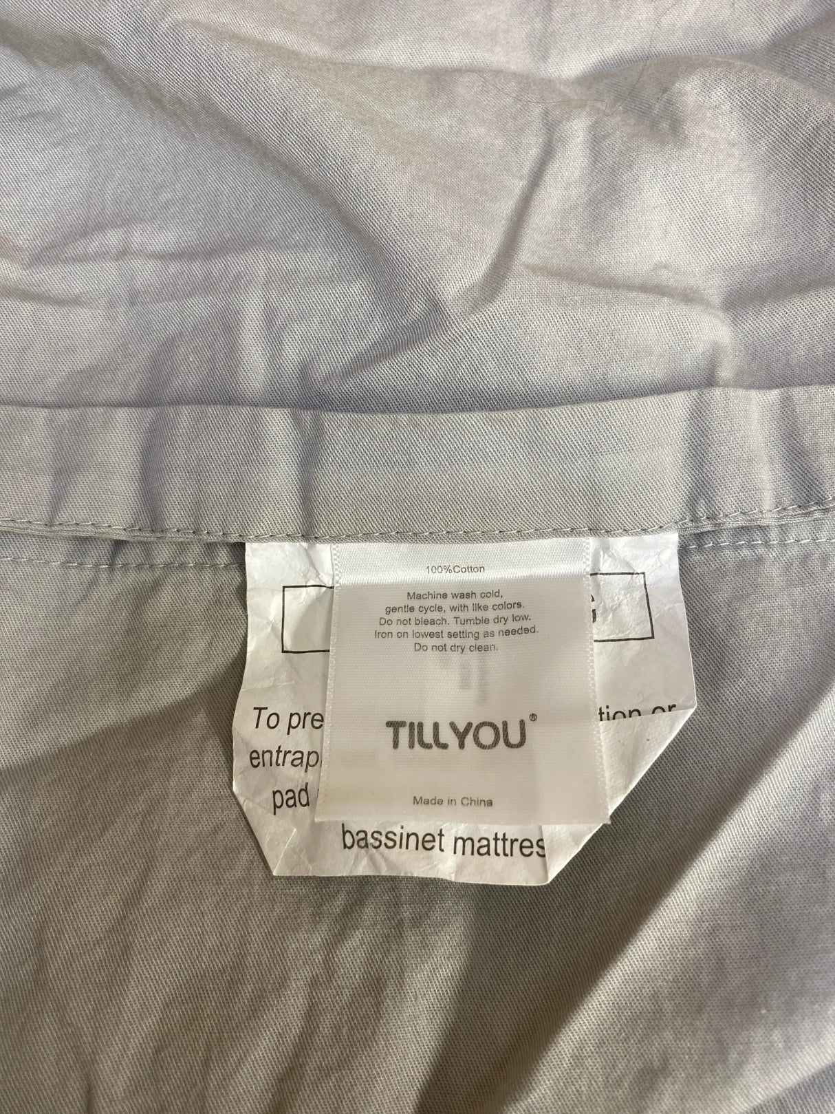 Tillyou bassinet mattress cotton fabric care label with washing instructions on gray textile