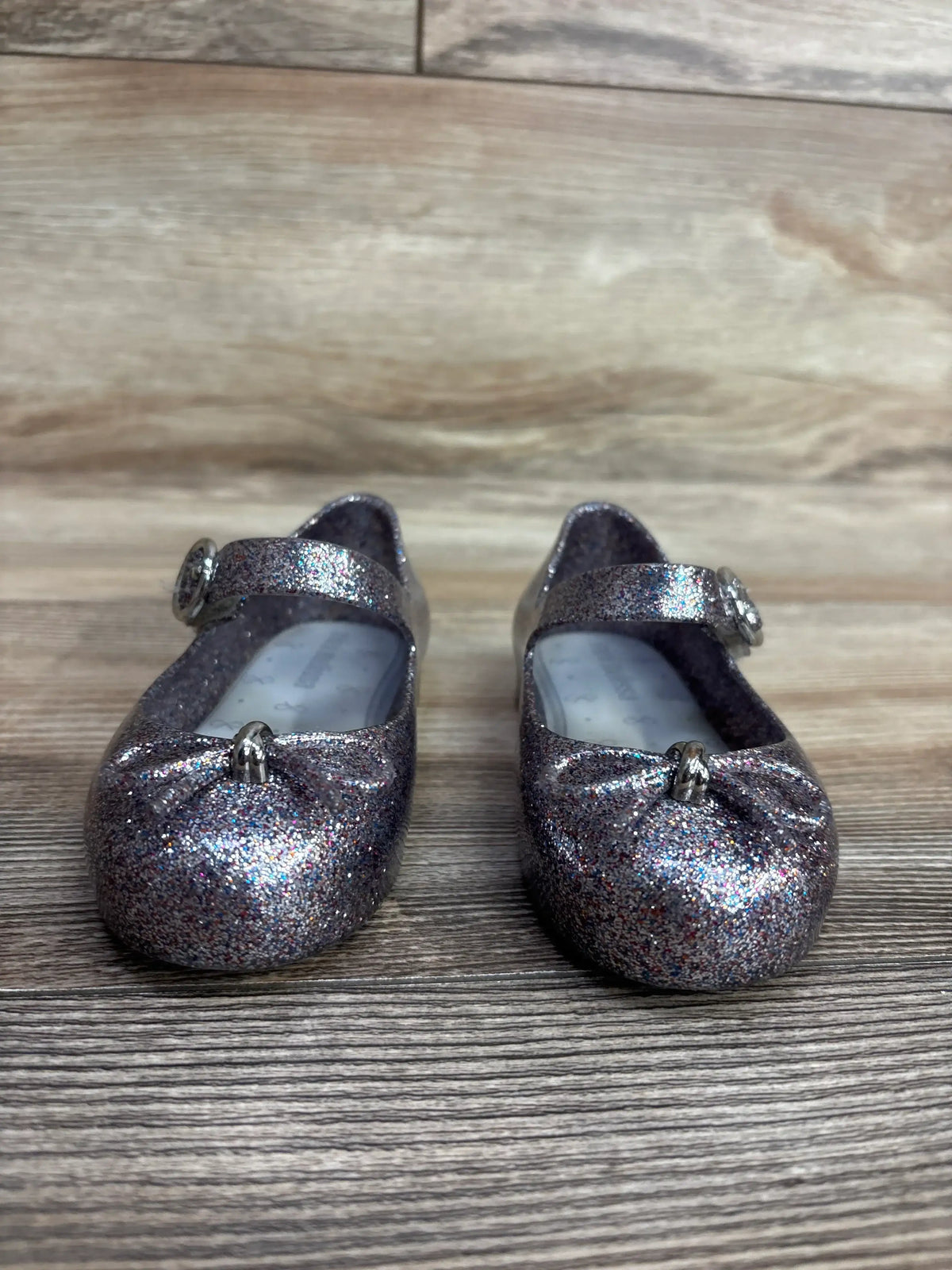 sparkly glittery silver Mary Jane baby shoes with bows on wooden surface