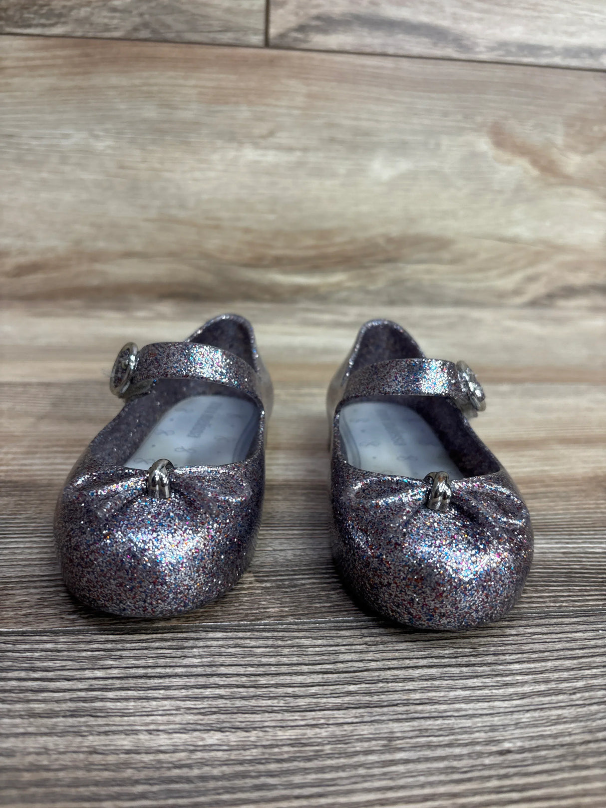 sparkly glittery silver Mary Jane baby shoes with bows on wooden surface