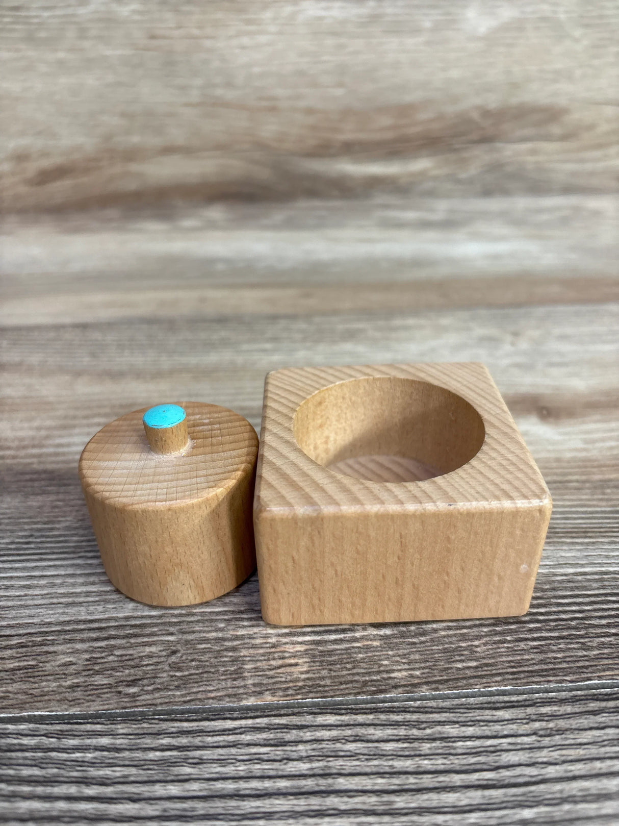 Wooden puzzle piece with square base and round peg with blue top on wooden surface