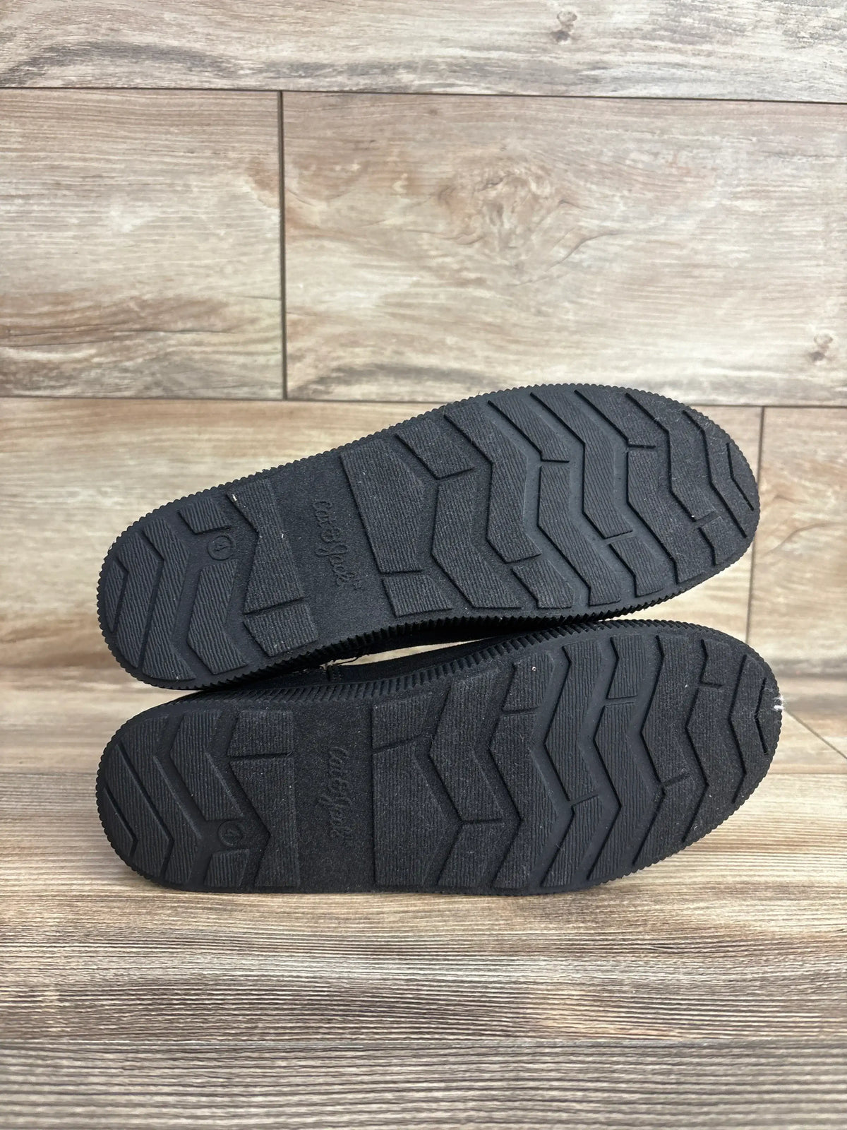 Black rubber soles of kids' shoes with zigzag tread on wooden floor background