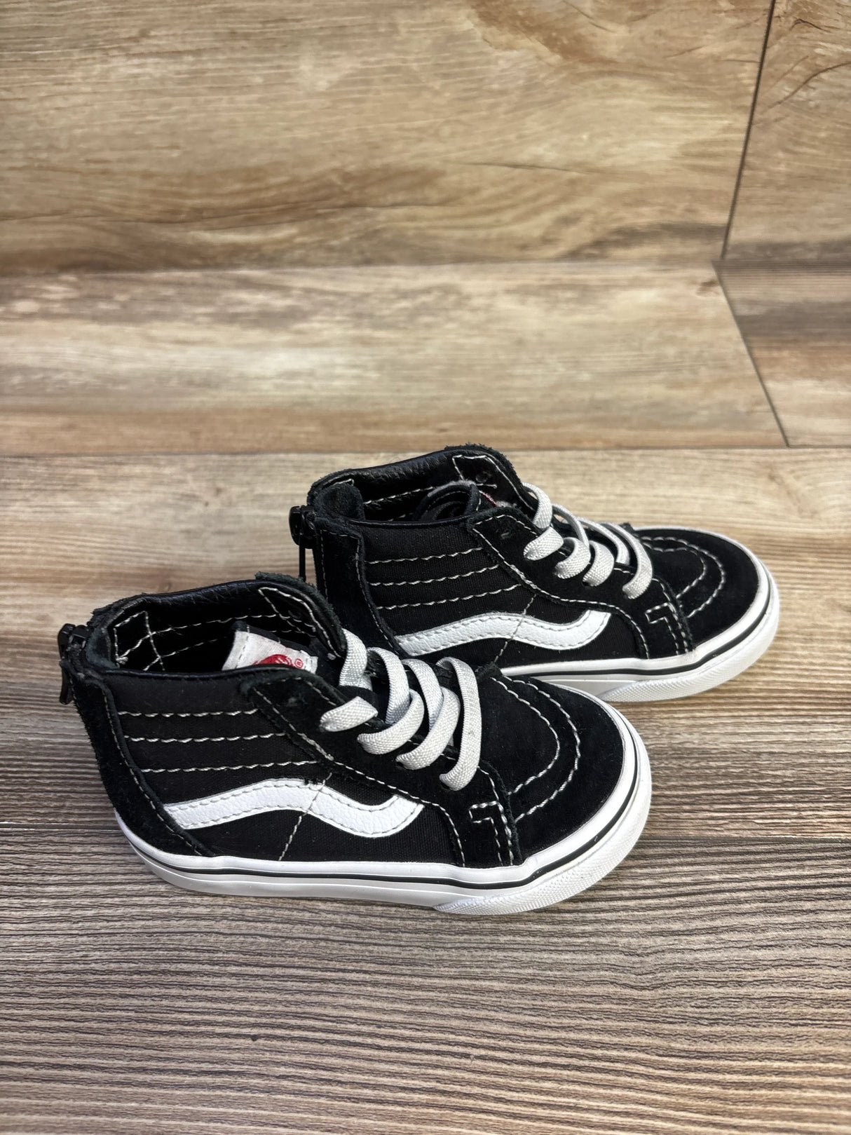 Angled side-top view of toddler Vans Sk8-Hi high-top sneaker showing white side stripe, white laces and back zipper pull on wood surface