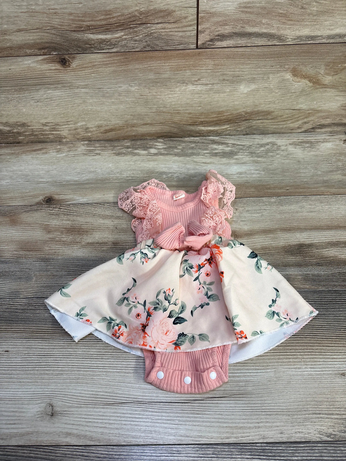 Flat lay of Karwuiiio Ribbed Lace Floral Bodysuit Dress pink sz 9-12m showcasing rose print skirt and bow on wood floor