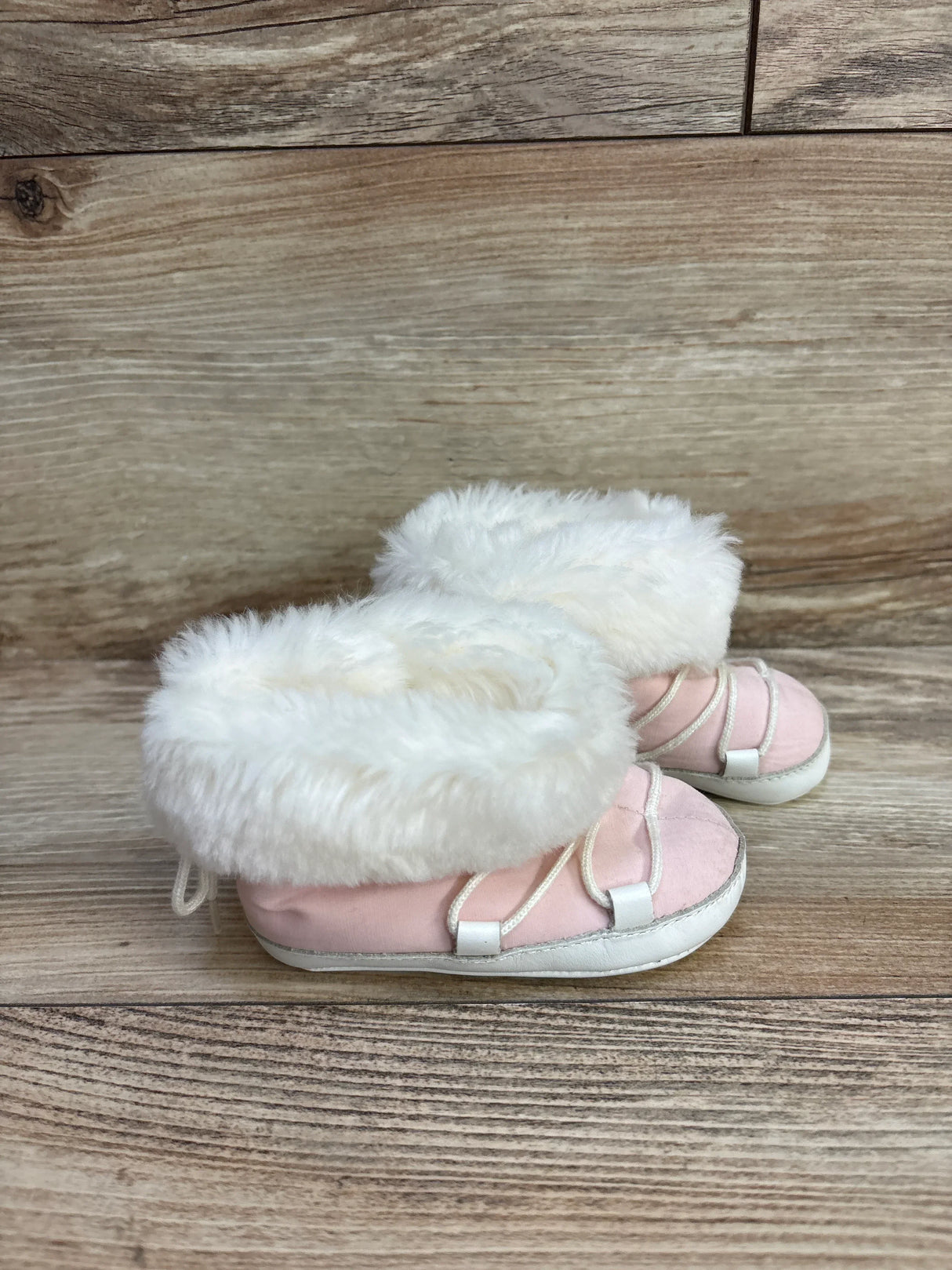 Pink baby booties with white faux fur trim on wooden background