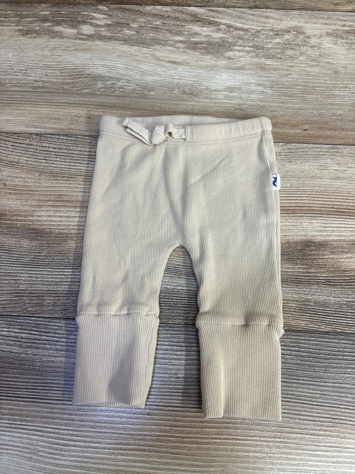 Front view of tan Grenalito newborn leggings showcasing ribbed fabric and drawstring waist on a wood-grain surface