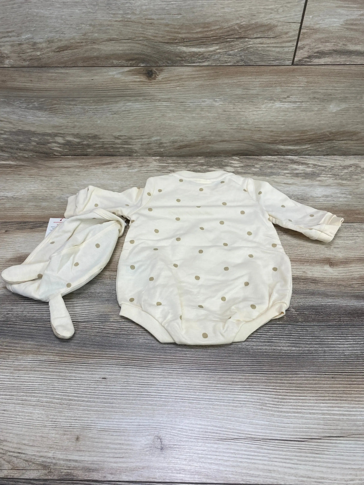 Flat lay of Cat and Jack cream baby romper with matching bonnet, gold polka dots on wood background
