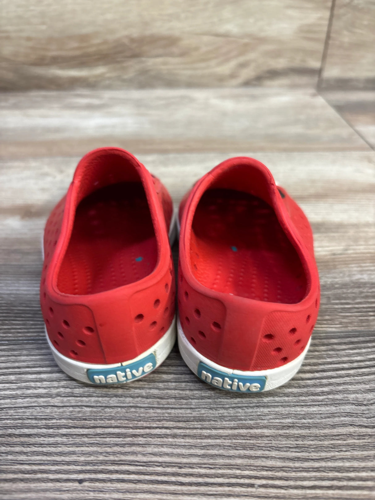 Back view of red Disney x Native Jefferson slip-on toddler shoes with perforated upper and white soles on wood floor