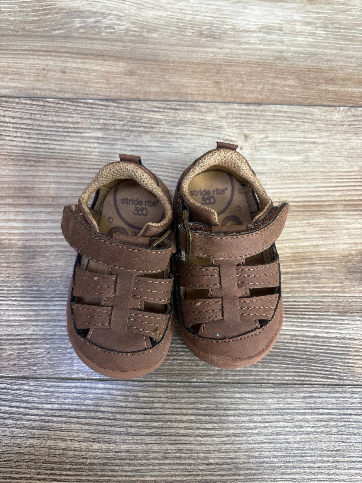 Brown Stride Rite Amos 3.0 fisherman sandals for toddlers on a wood grain surface.