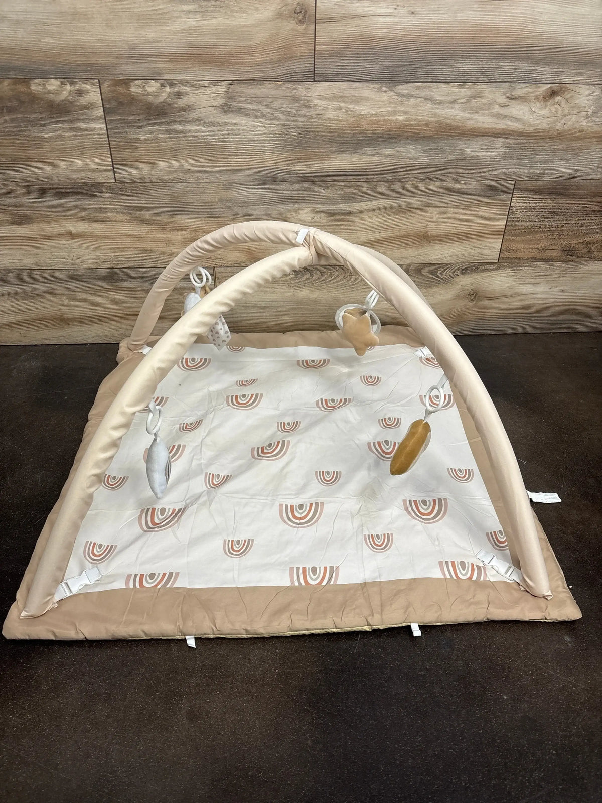 Front view of Mallify Tummy Time Play Gym Rainbow showcasing beige arches with hanging toys over rainbow print padded mat on wood plank floor