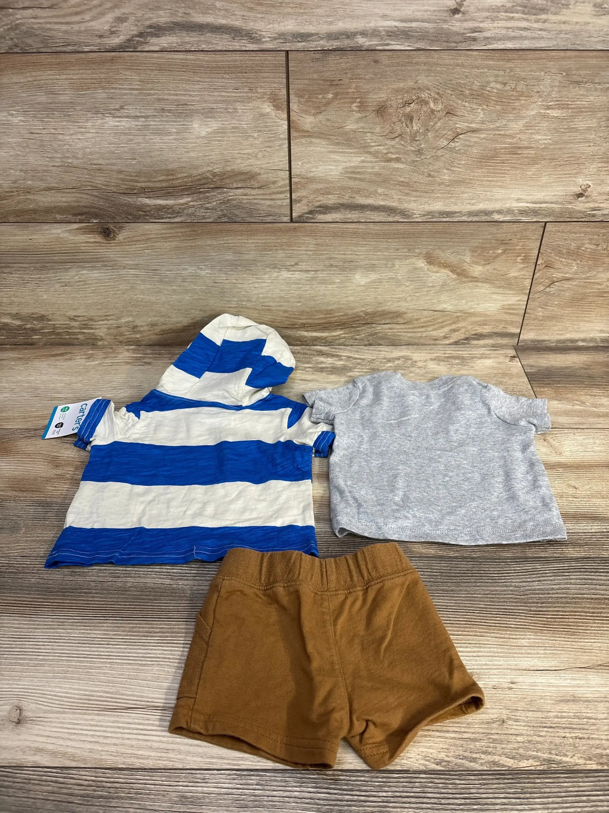 Flat lay of Carter's 3pc shirt and shorts set showing blue-and-white striped hooded top and brown elastic shorts on wood floor