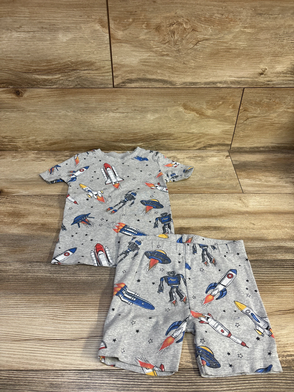 Flat lay of Member’s Mark 2-piece grey toddler pajama set (4T) showing rockets, robots, and UFOs on wood background