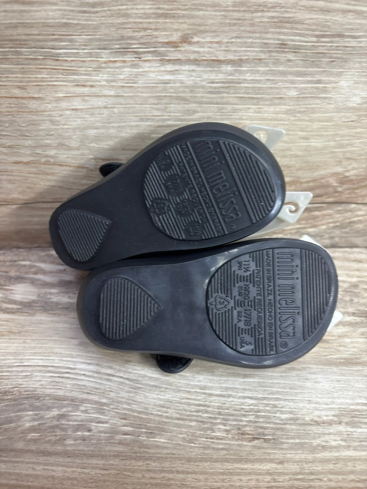Bottom view of Mini Melissa Ultragirl Bow black jelly flats showcasing textured soles on a wooden surface