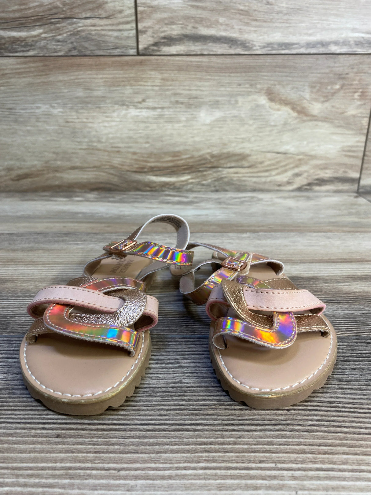 Girls’ tan sandals with pink iridescent straps, toddler size, on wooden background