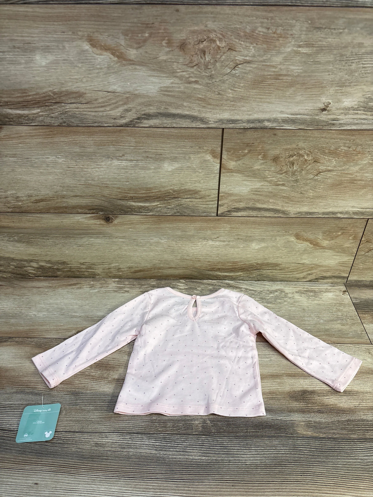 Back view of Disney Baby pink long-sleeve polka dot shirt showcasing keyhole button closure and small silver dots on wood background