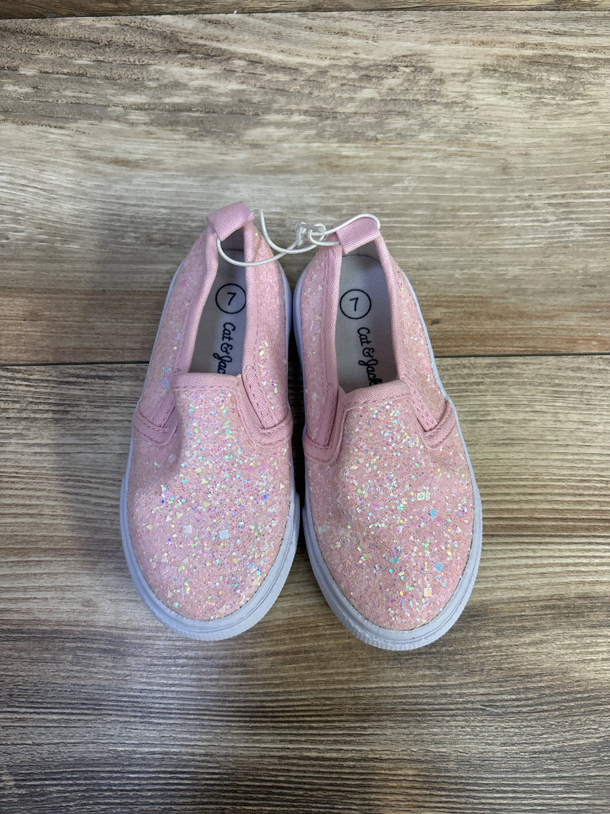 Top-down view of Cat and Jack Yana pink glitter slip-on sneakers showing iridescent glitter and white soles on wood floor