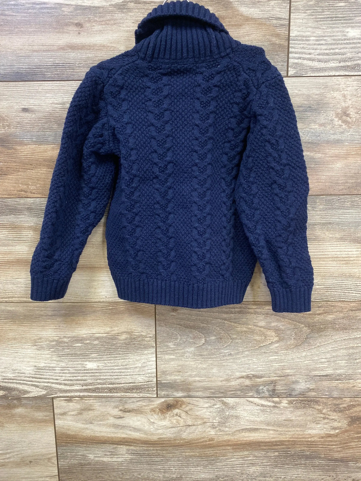 Back view of Janie & Jack navy cable-knit toddler cardigan, size 4T, showing folded shawl collar on wood floor