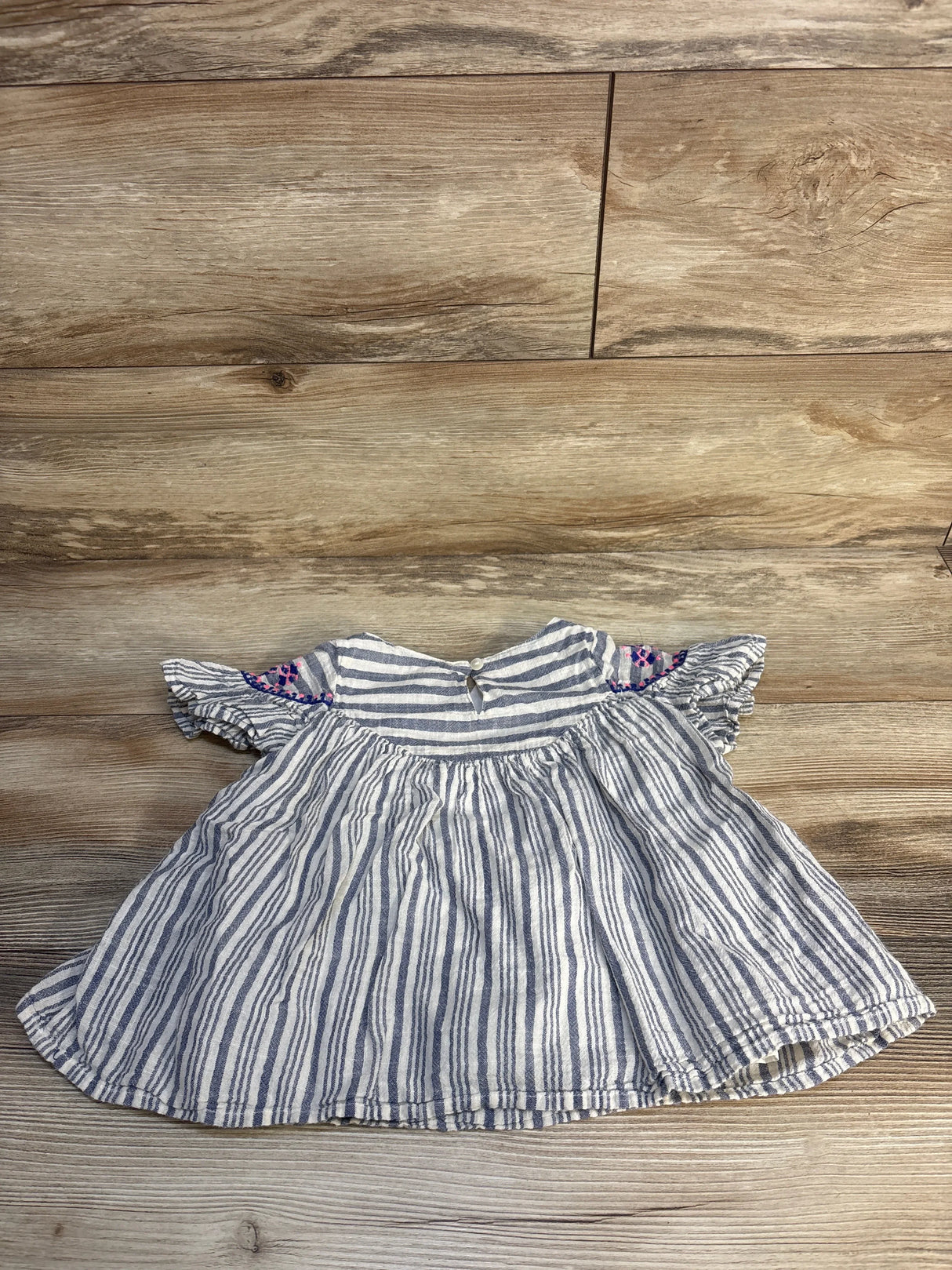 Striped short sleeve baby dress with ruffle sleeves and embroidered shoulder detail on wood floor