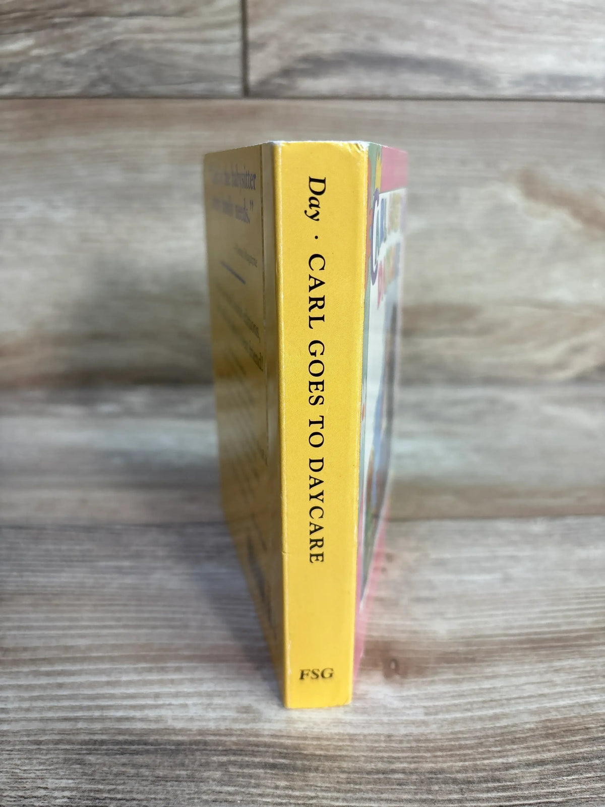 Side view of Carl Goes to Daycare board book showing its yellow spine on a wood-grain surface