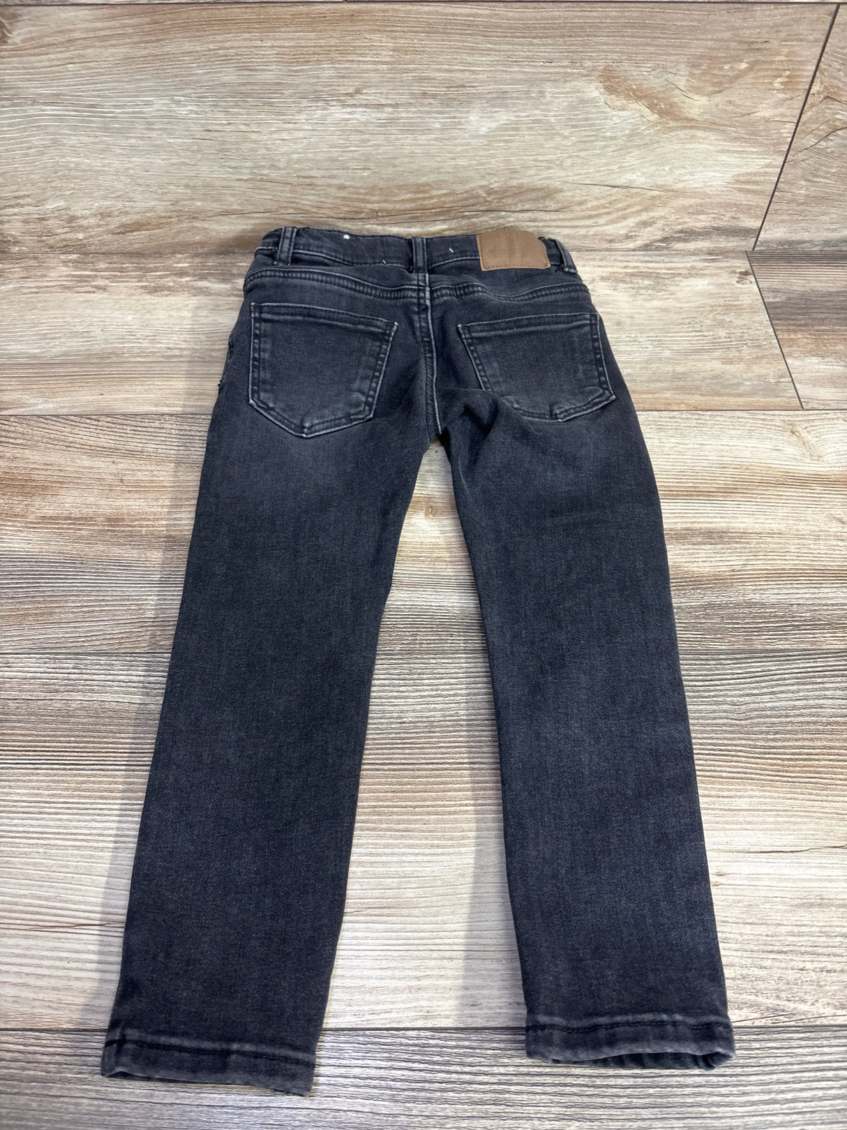 Pair of black kids jeans with back pockets on wood floor