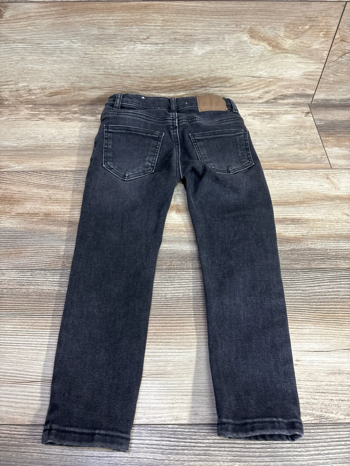 Pair of black kids jeans with back pockets on wood floor