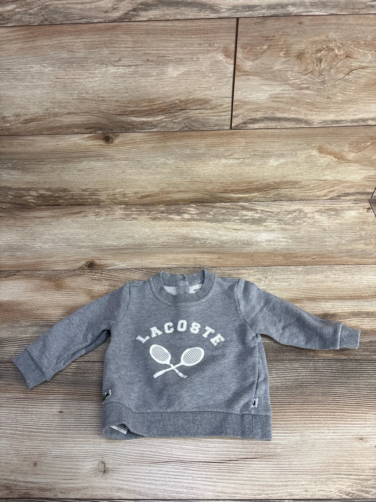 Gray Lacoste toddler sweatshirt with white tennis racket print on wood floor background