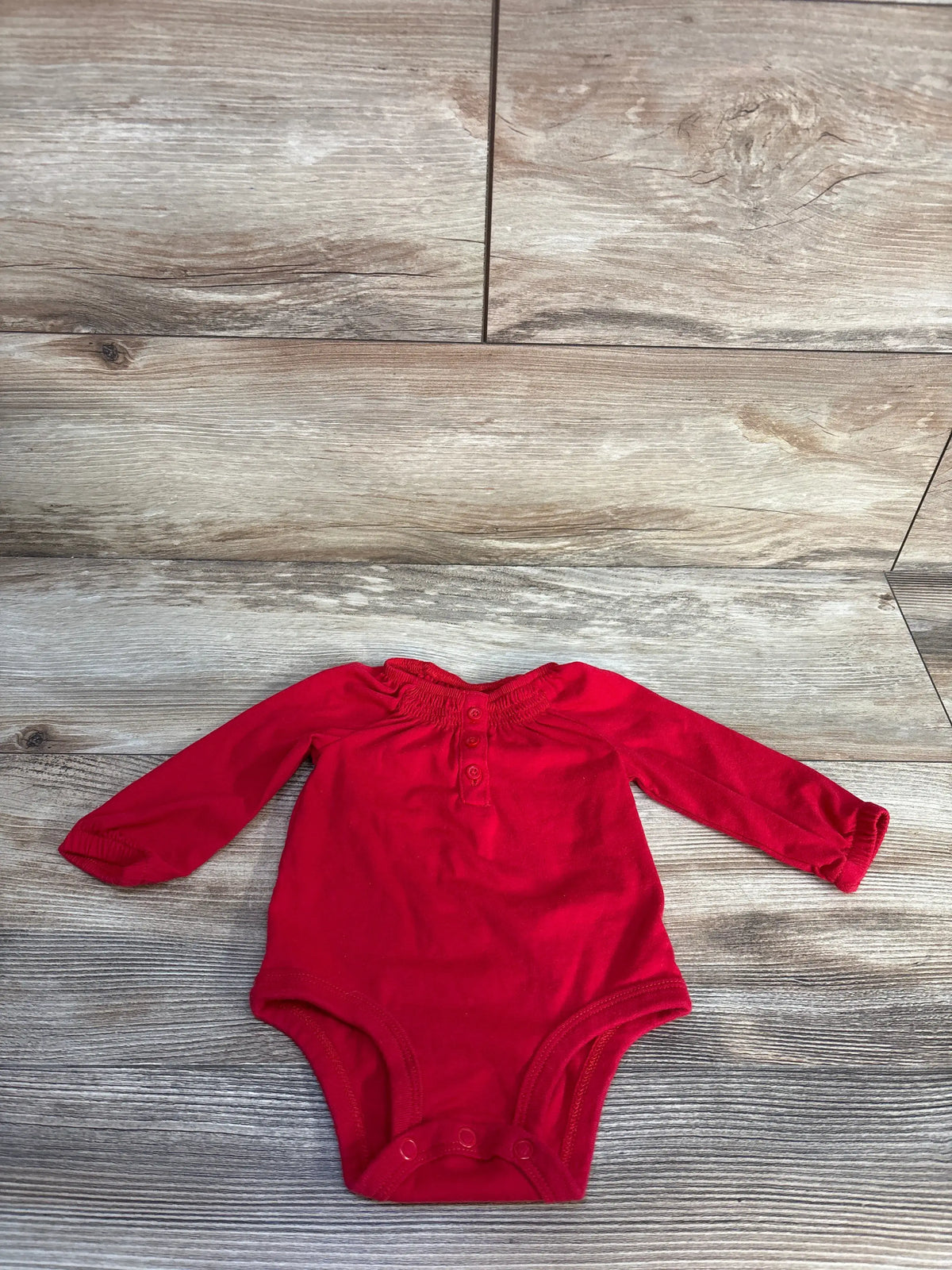 Front view of Oshkosh red long sleeve henley bodysuit showcasing button placket and bottom snaps on wood flooring