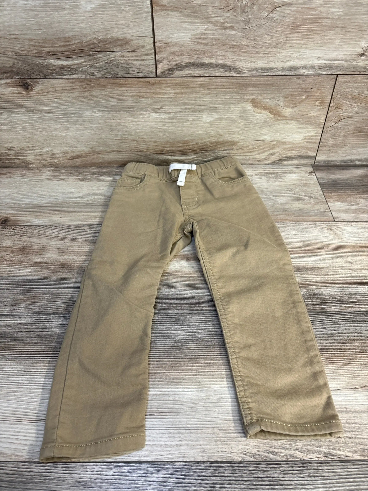 Kids khaki pants with white drawstring, laid on wooden floor