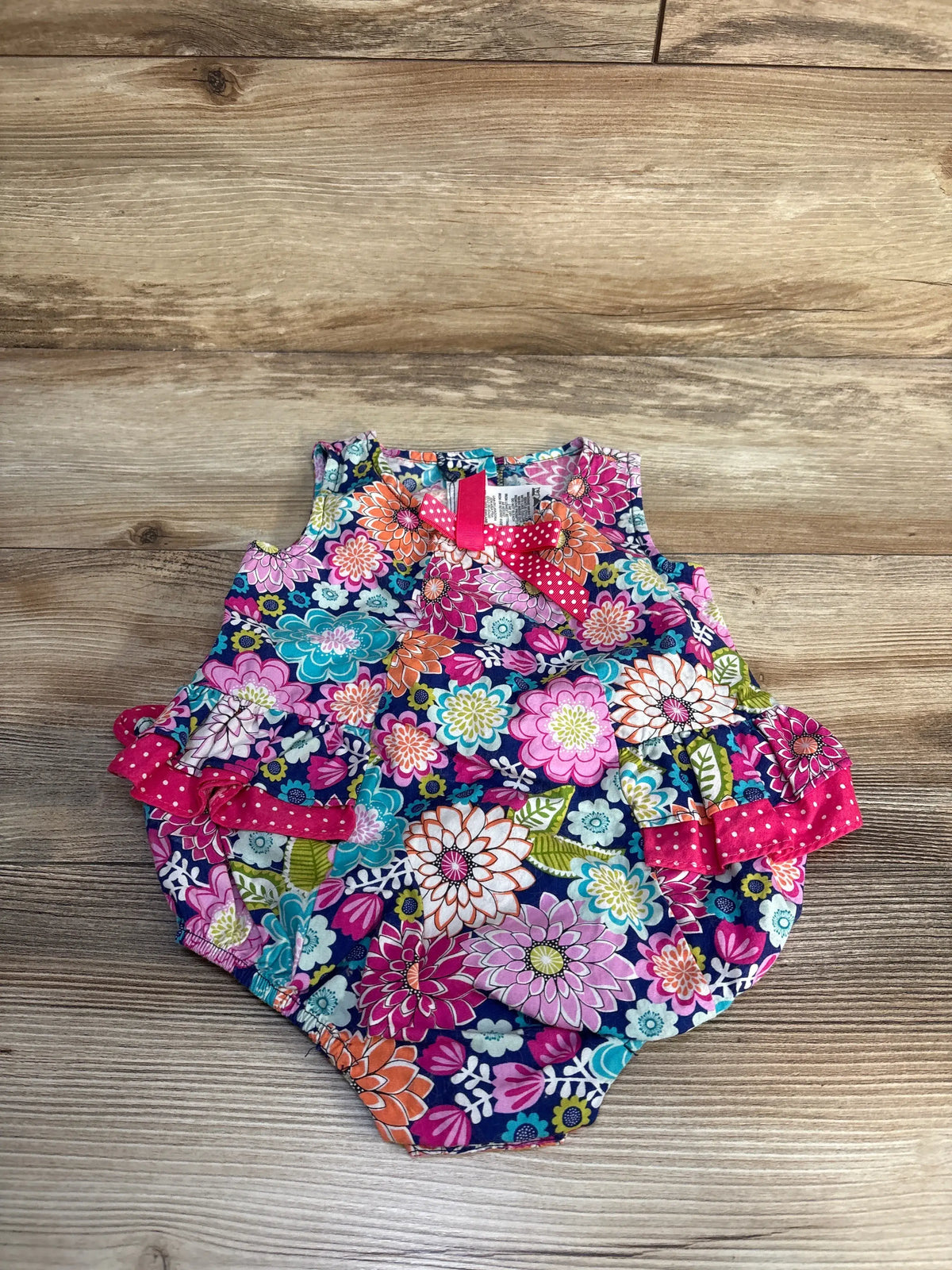 Front view of Bonnie Baby floral bubble romper showcasing multicolor flowers and polka-dot trim on a wood background