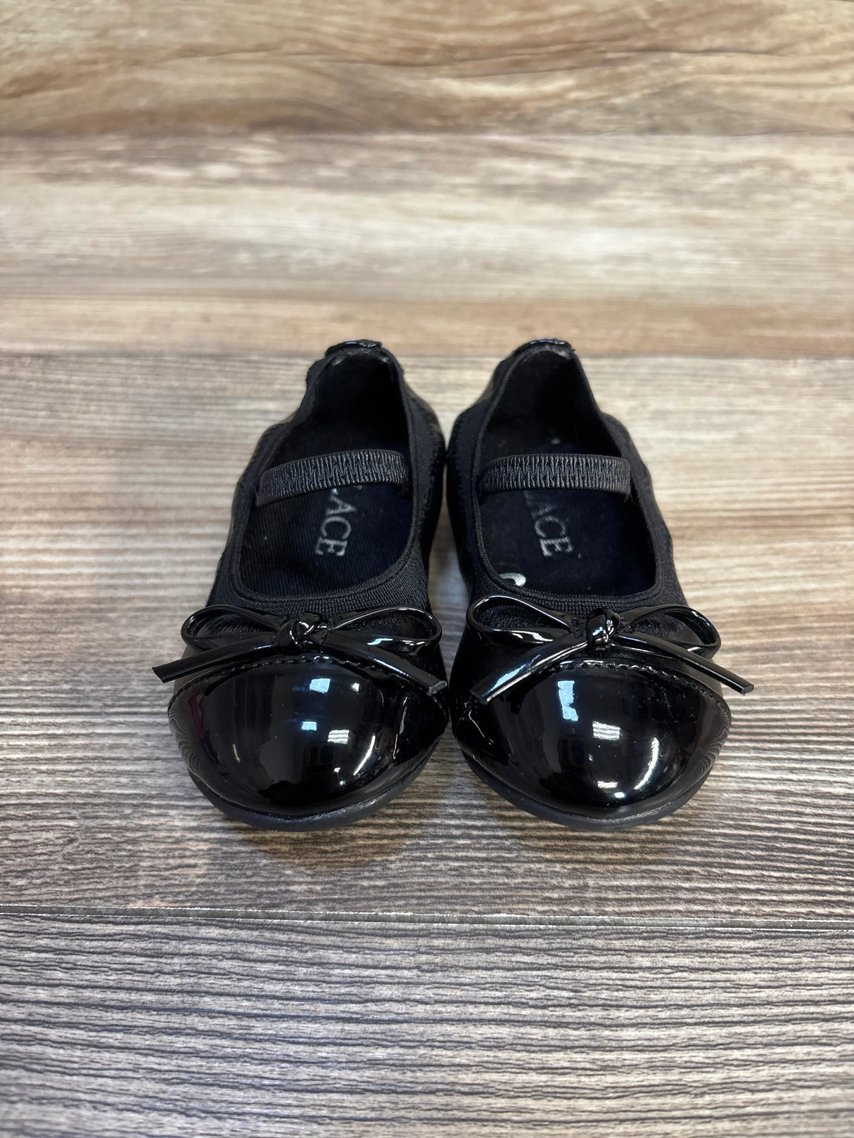 Black toddler Mary Jane shoes with bows and elastic strap on wood floor