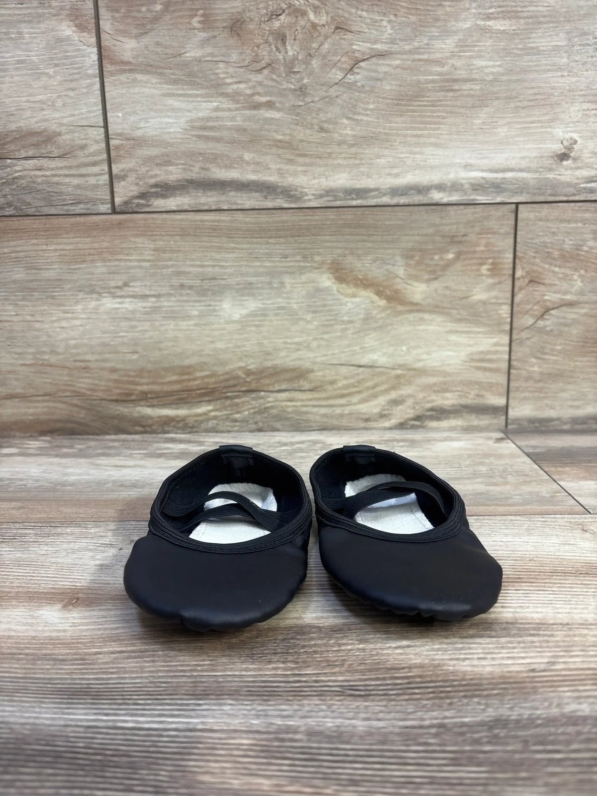 Front view of Stelle black toddler ballet shoes showcasing elastic strap and rounded toe with wood floor background