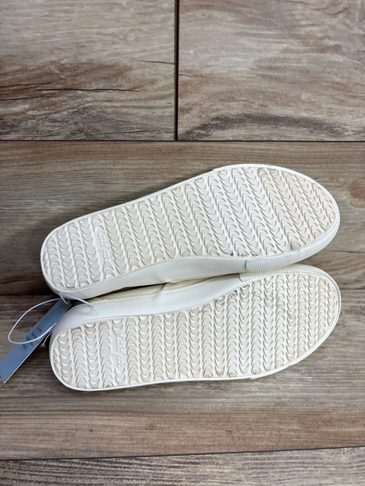 Bottom view of Cat & Jack Tyler slip-on sneakers (off-white, size 6Y) showing textured rubber soles on wood floor