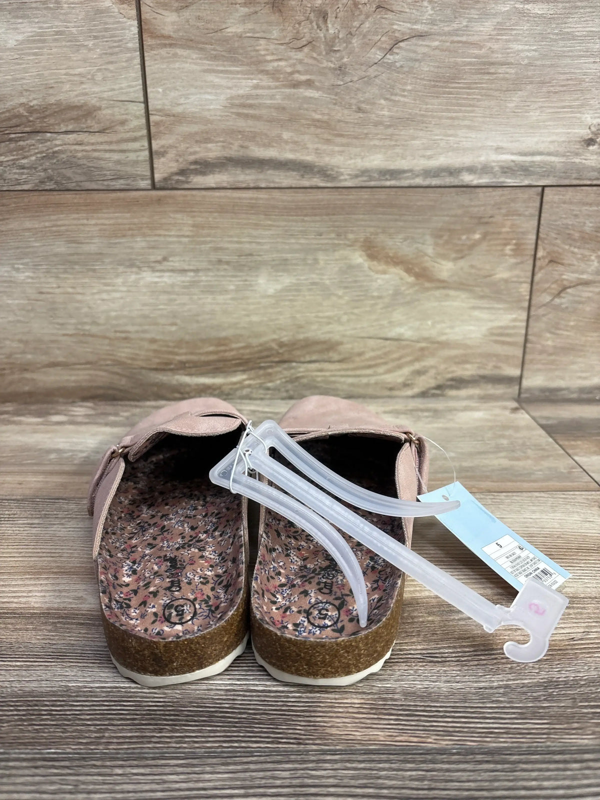 Rear view of Cat & Jack Perry clogs in blush showing floral printed insoles, cork soles, and attached retail tag on wooden floor