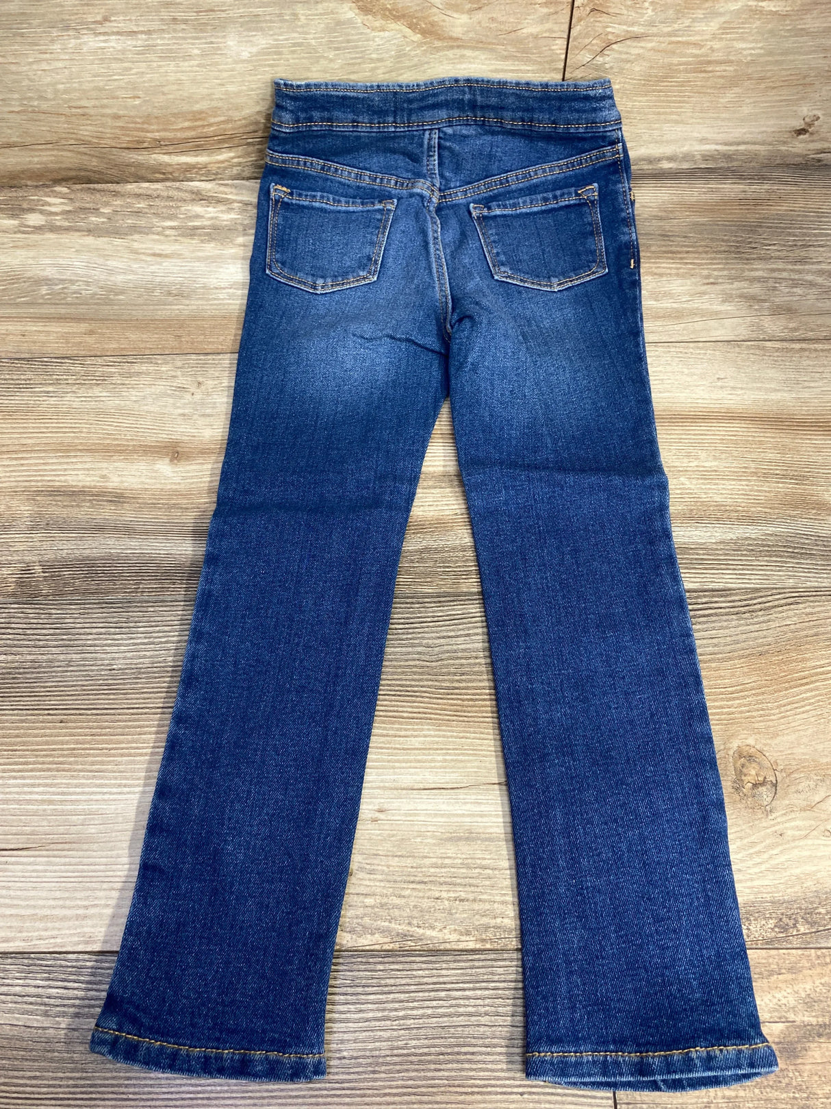 Kids blue denim jeans, straight leg, back pockets, laid flat on wood background