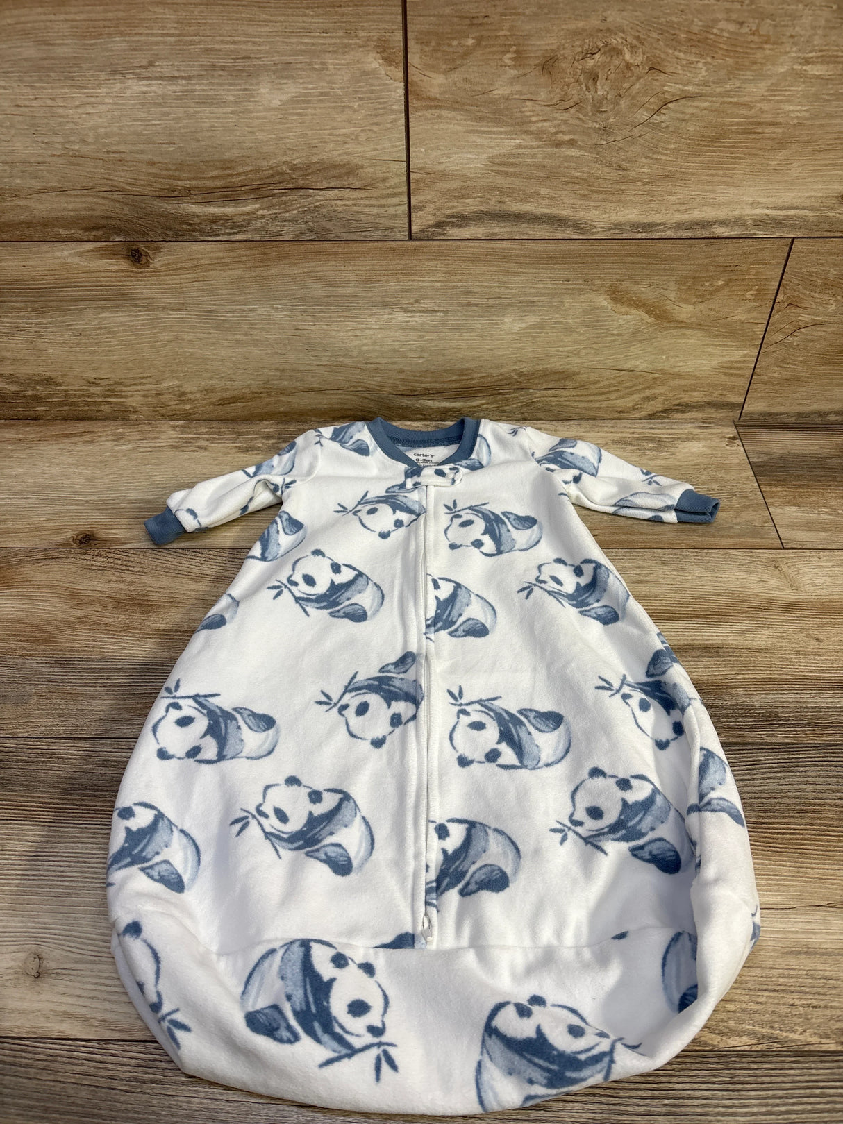 Top-down view of Carter’s white panda-print sleep sack showing front zipper, long sleeves with blue cuffs, and rounded bottom on wood floor