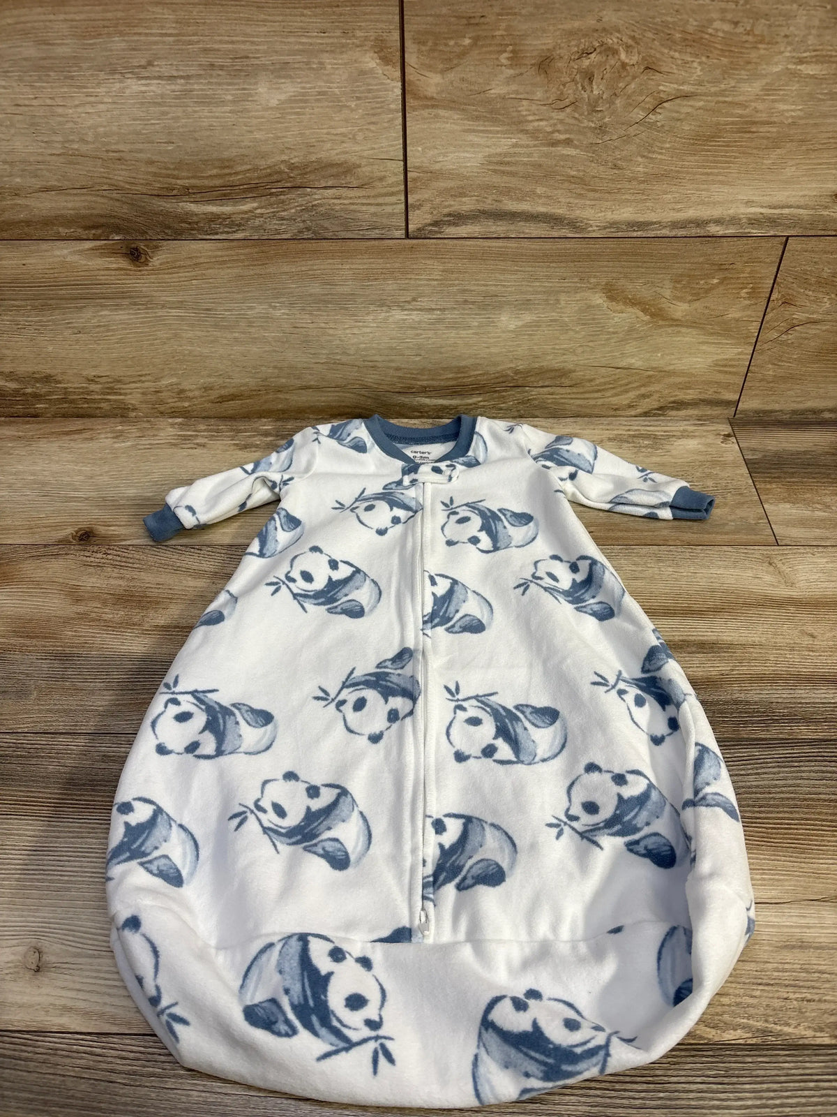 Top-down view of Carter’s white panda-print sleep sack showing front zipper, long sleeves with blue cuffs, and rounded bottom on wood floor