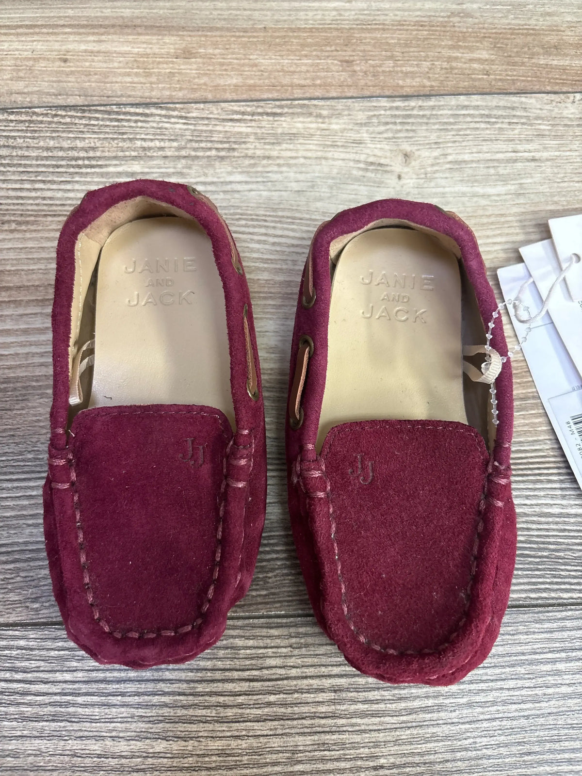 Pair of burgundy suede Janie and Jack kids moccasin shoes on wood surface
