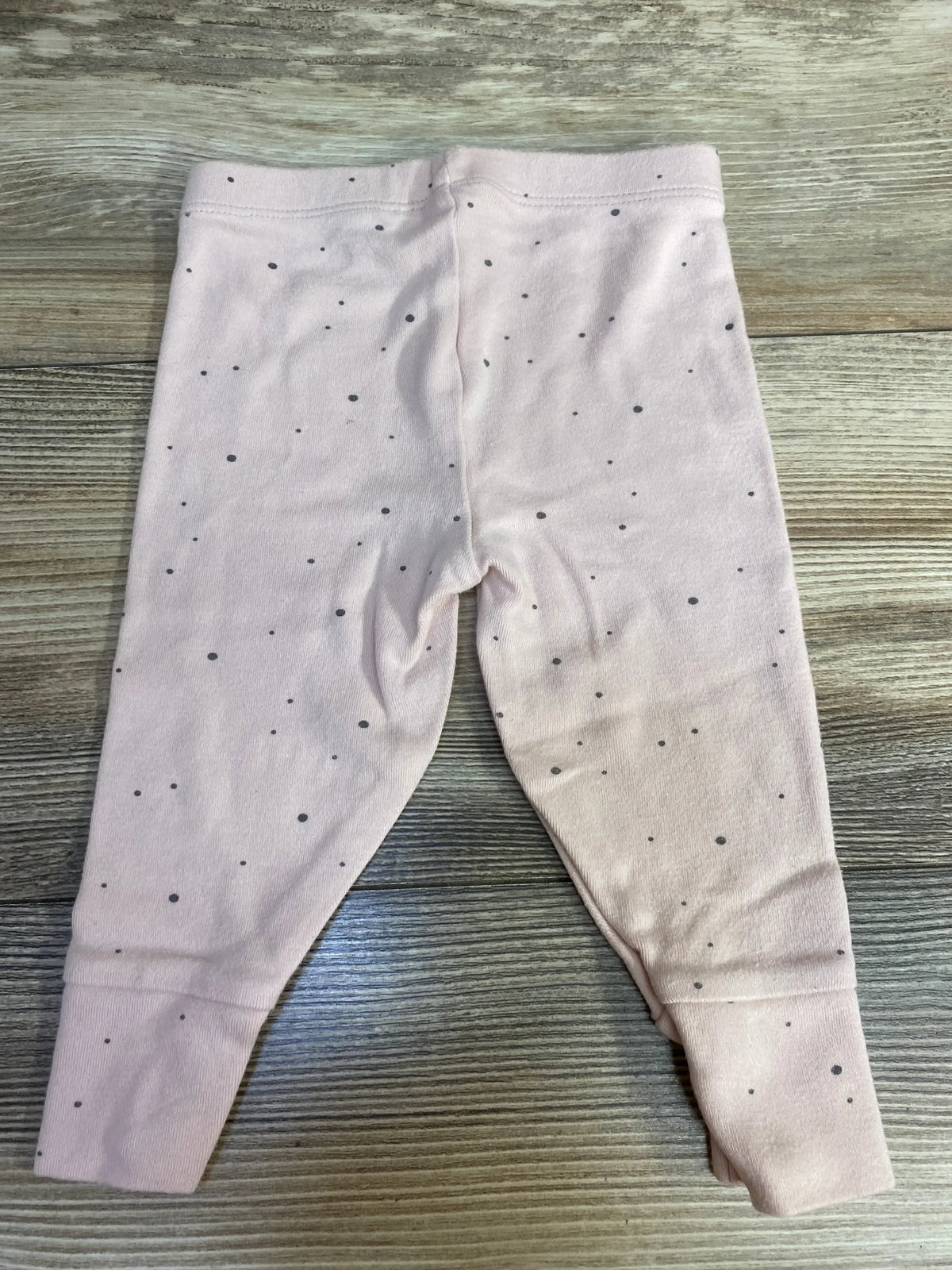 Light pink baby leggings with small black dots on wooden surface