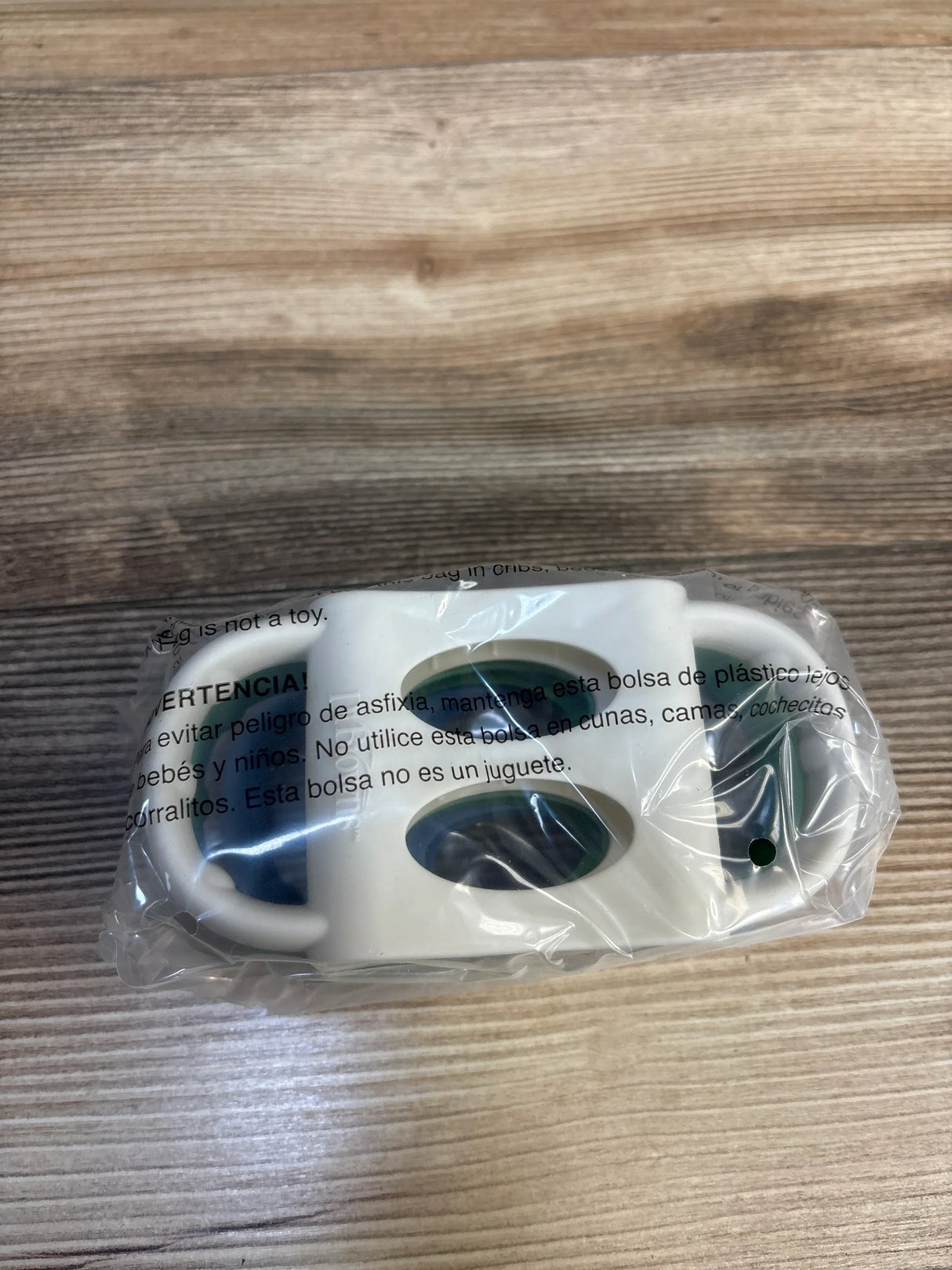 Top-down view of Dr. Brown’s Milestones silicone narrow baby bottle handles in clear plastic packaging showing white oval grips on wood surface